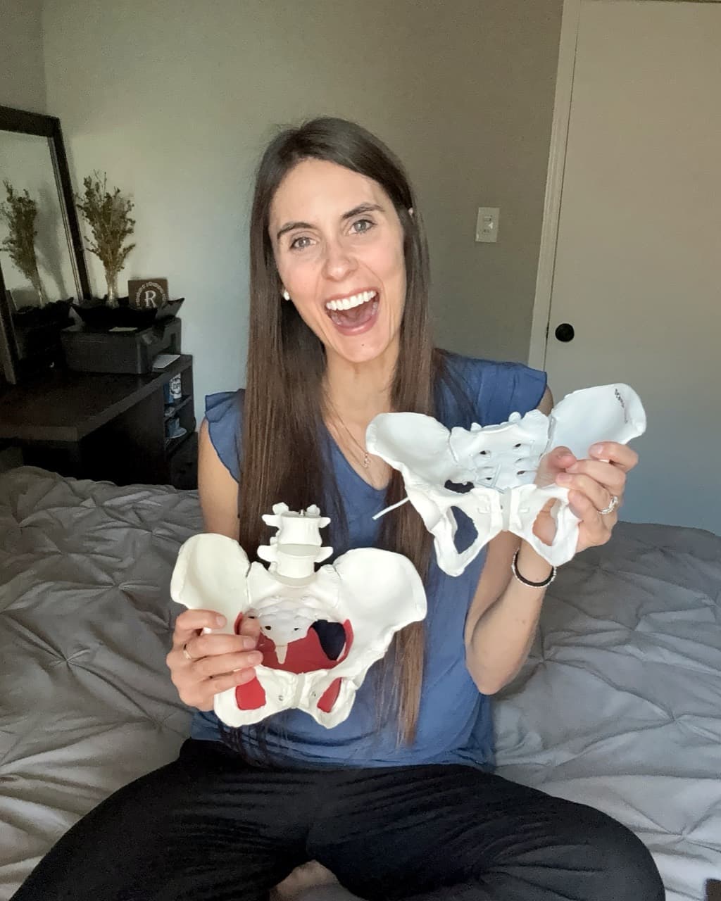 Deborah Reddout smiling and holding two anatomical pelvis models